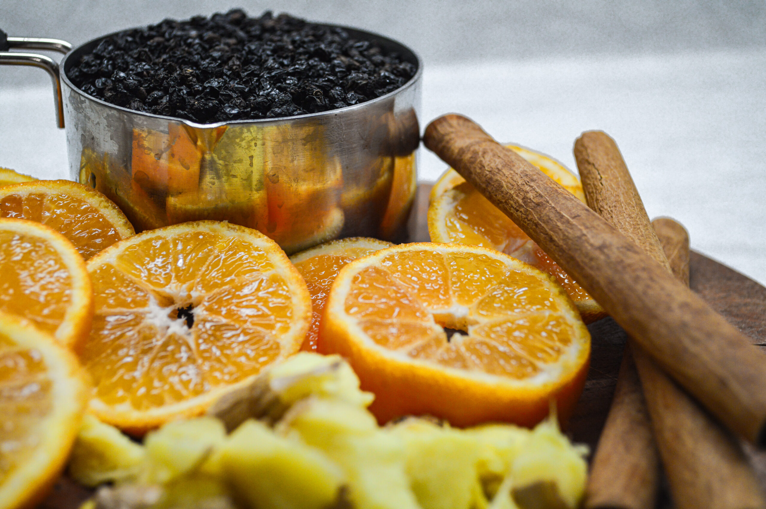 Herbal homemade elderberry syrup ingredients — sliced oranges, chopped ginger, cinnamon sticks and 1 measuring cup full of dried elderberries