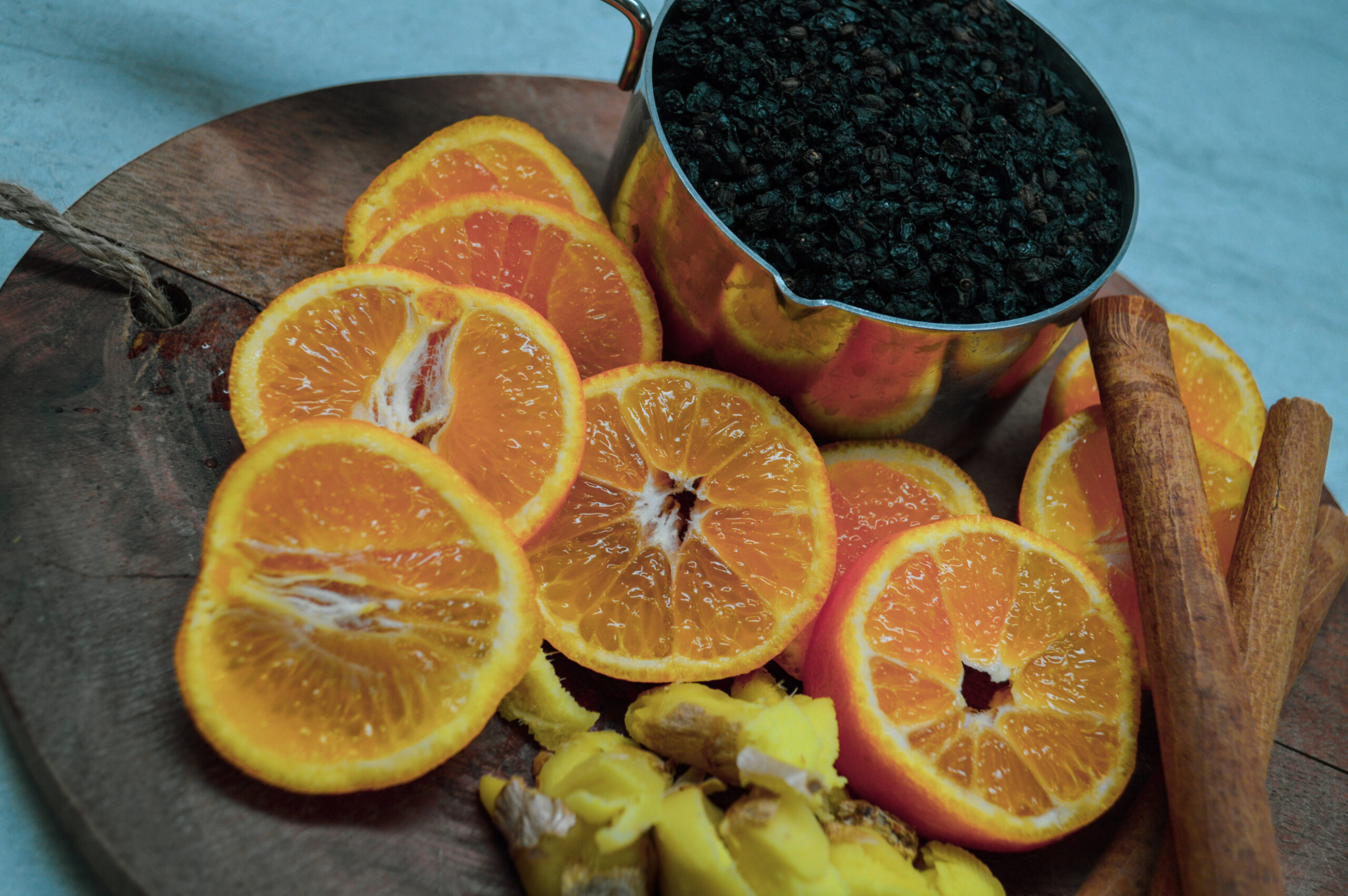 sliced oranges, chopped ginger, cinnamon sticks and 1 measuring cup full of dried elderberries laid out on a cutting board.