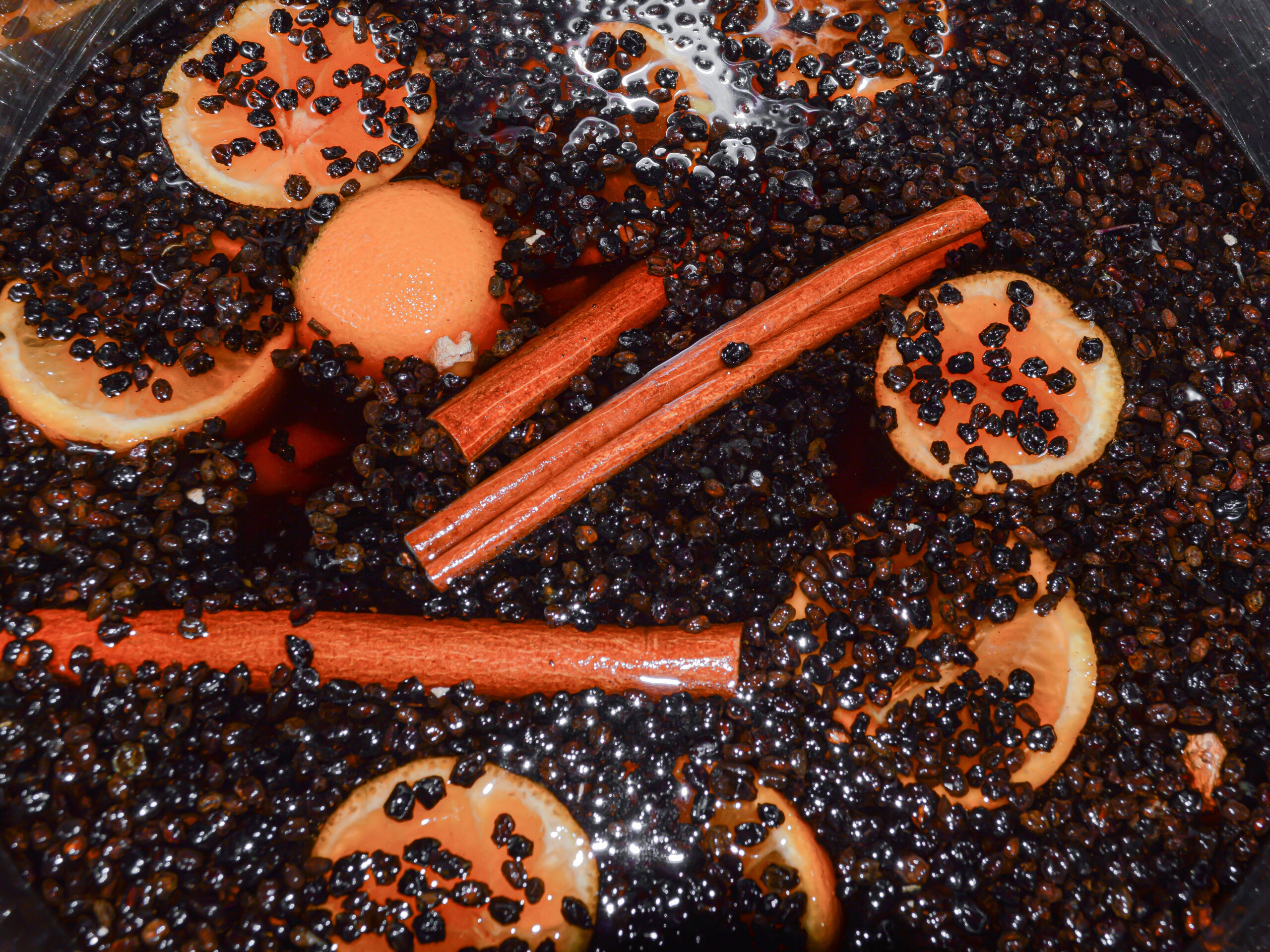 Dried elderberries, sliced oranges, cinnamon sticks stewing in a pot full of water.