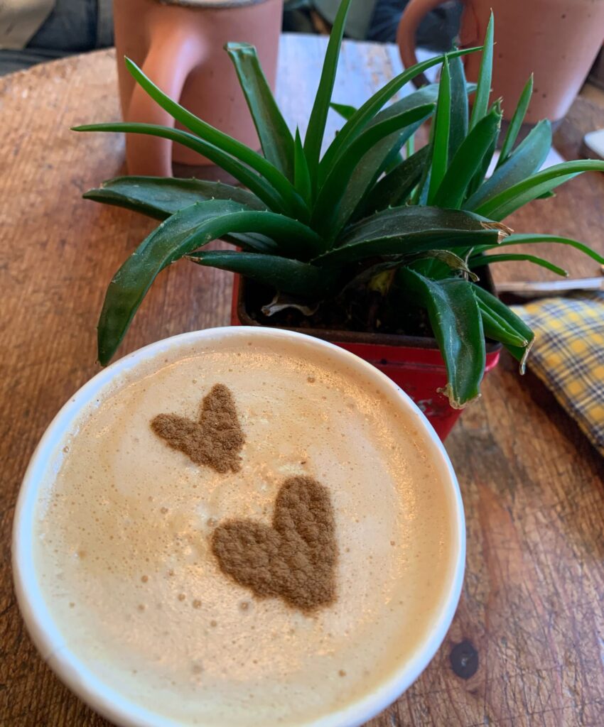 Coffe with coffee art heart on a table with a plant and 2 cups.