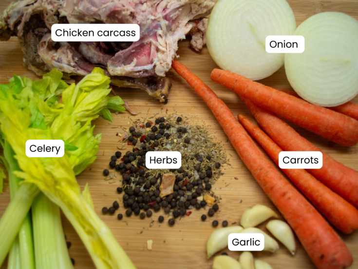 Chicken carcass, onion, carrots, celery, garlic and herbs laid on a wooden cutting board