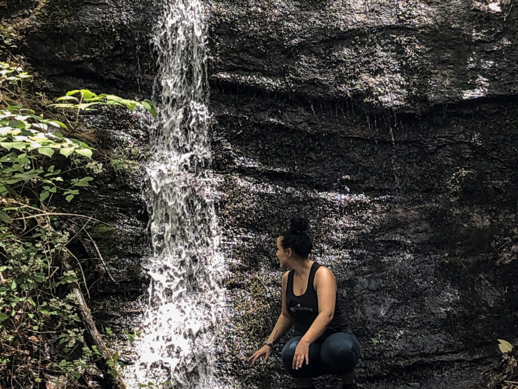 Woman enjoying a slow moment connecting with nature squared next to a waterfall