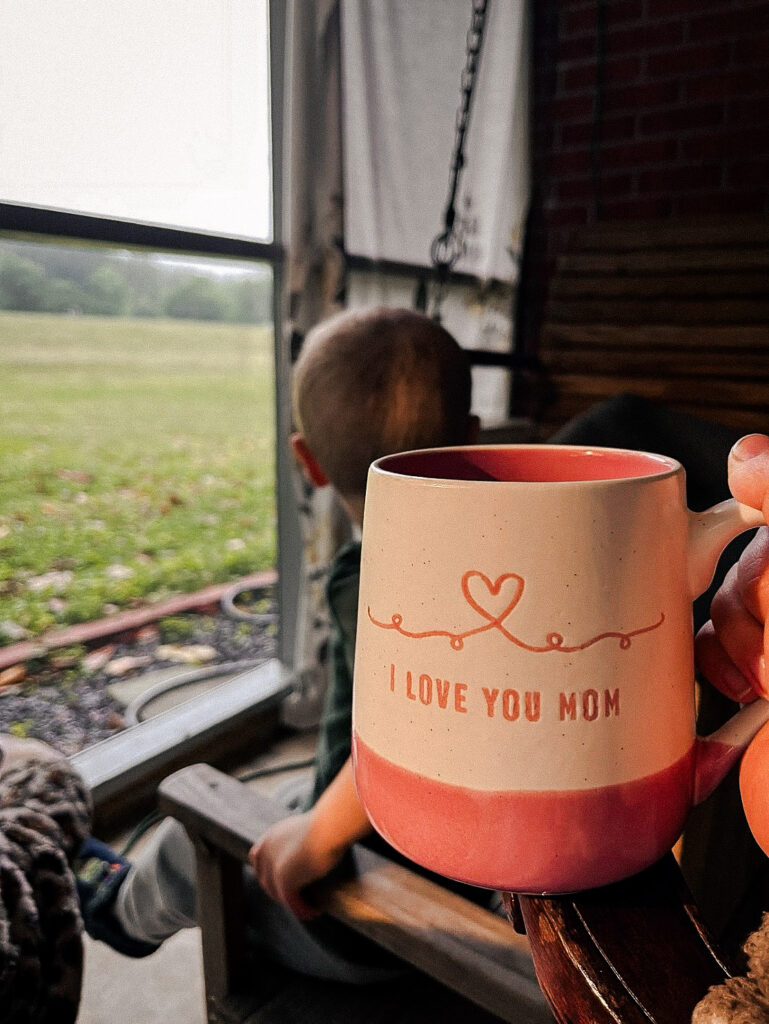 tired mom holding I love you mom coffee mug enjoying slow moment on the porch with son