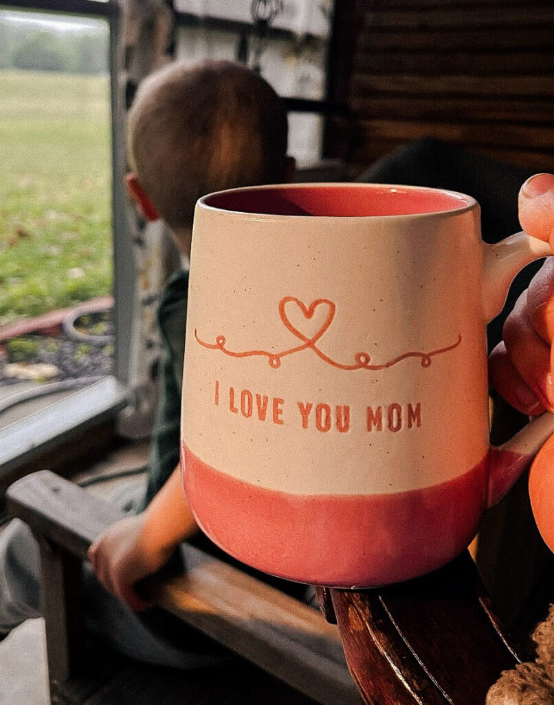 tired mom holding I love you mom coffee mug enjoying slow moment on the porch with son